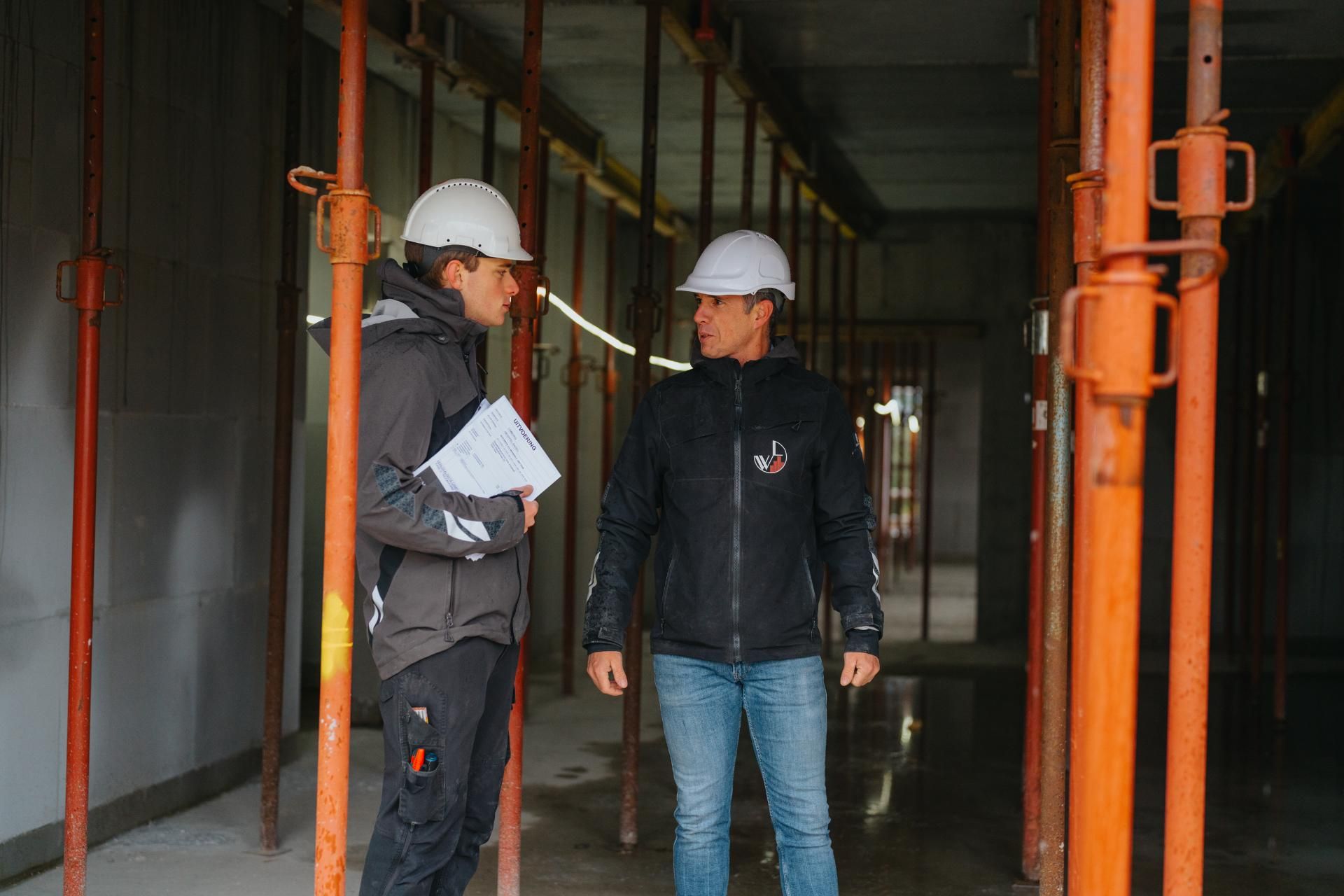 Twee bouwvakkers met helmen onderzoeken een bouwplaats.