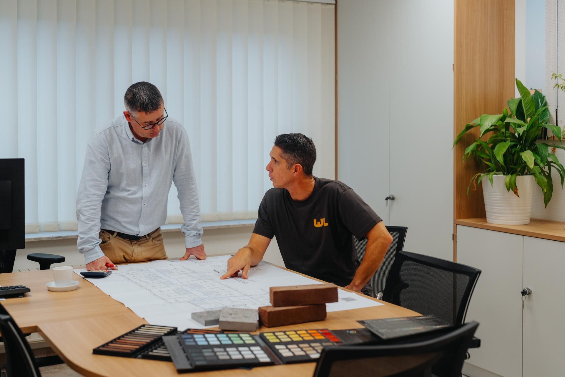 Twee mannen zitten rond een tafel en bekijken architectonische plannen.